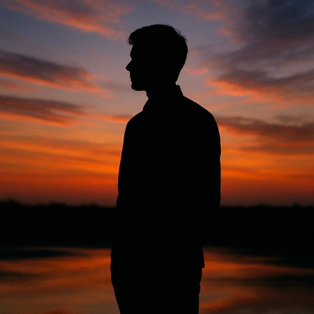 Silhouette of a man standing against a sunset sky background.