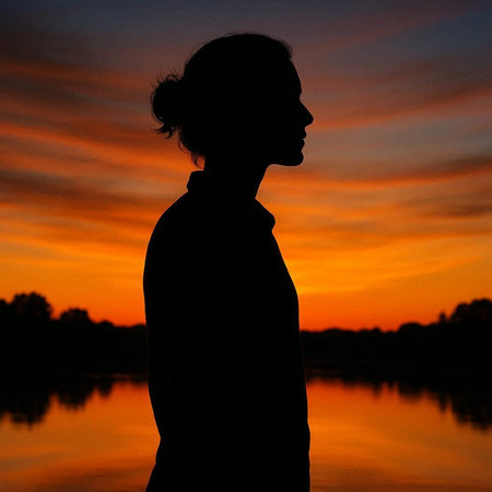 Silhouette of a young man standing in front of a lake at sunset