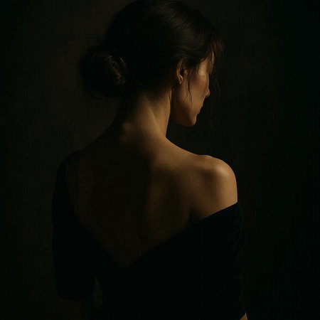 Back view of young beautiful woman in black dress on dark background.