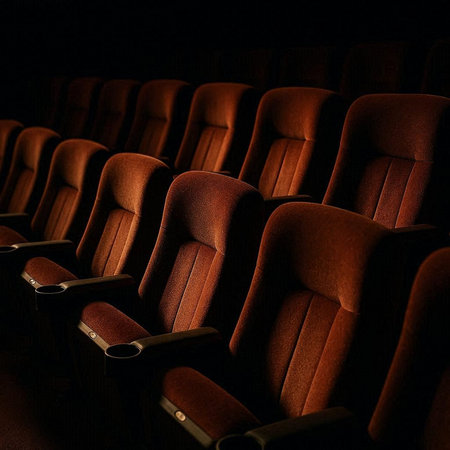 Movie theater auditorium with rows of red leather seats illuminated by the spotlight.