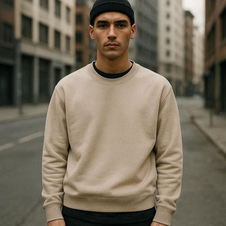 Fashionable young man in a beige sweatshirt with a black cap stands on the street.