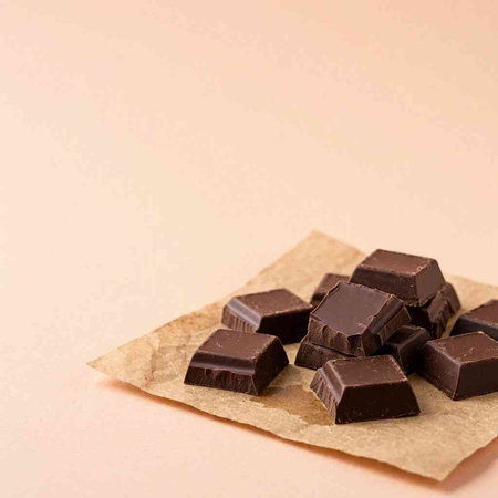Pieces of dark chocolate on a beige background. Copy space.