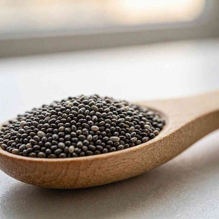 Black mustard seeds in a wooden spoon on a light background. Selective focus.