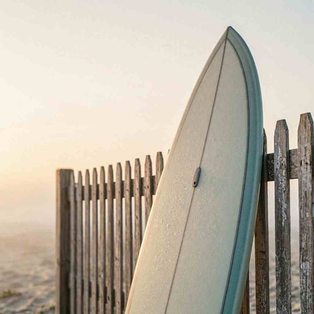 Surfboard leaning against a wooden fence on the beach at sunset