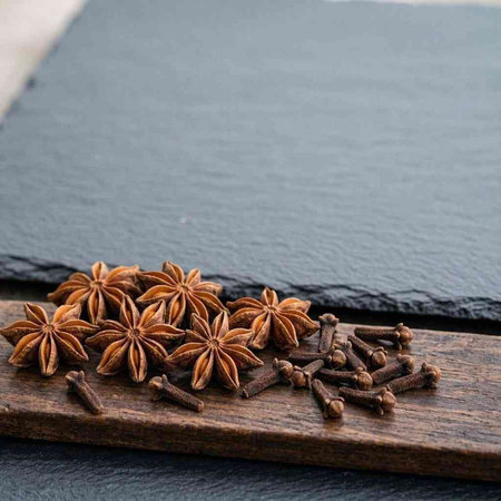 Star anise and cloves on a wooden board on a black background