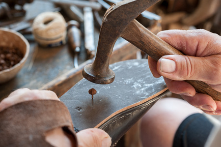 The shoemaker applies a bullet on the sole of a shoe. Various tools and instrument are placed on the work benchの写真素材