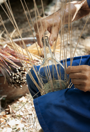 Basket maker creates a cover for a wine flaskの写真素材