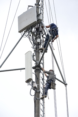 Two workers with harness climb up the ladder of the antenna towerの写真素材