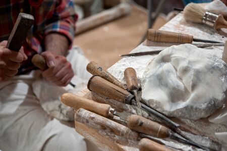 Sculptor working on alabaster sculpture in his workshop with hammer and chisel. Various tools on the bench.の写真素材