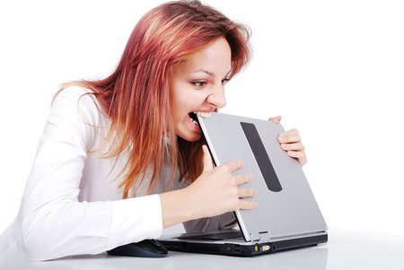 Crazy young woman is biting her laptop in officeの写真素材