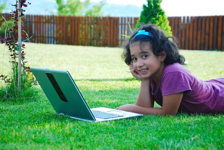 A little cute girl laying down in grass with laptopの写真素材