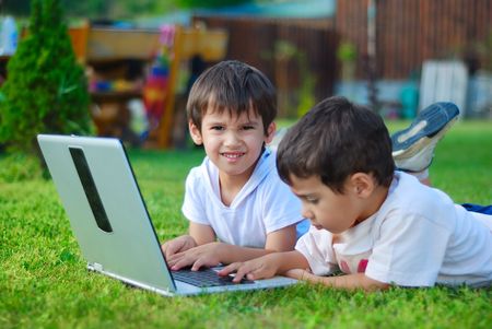 Two cute children laying in grass on laptopの写真素材