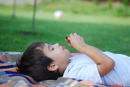 Cute kid is laying and eating fruit in beautiful environmentの写真素材