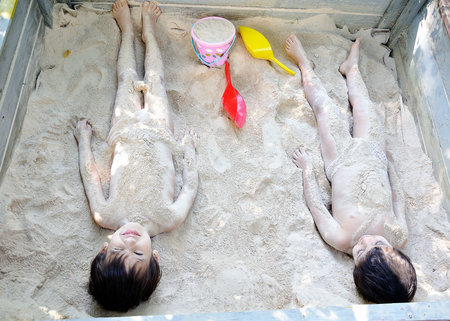 Two male children playing in sand, hiding and covering themselfsの写真素材