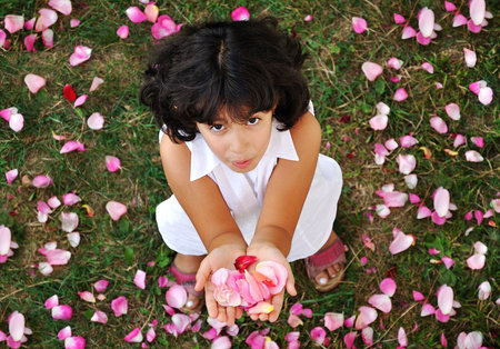 A little cute girl in white holding roses in handsの写真素材