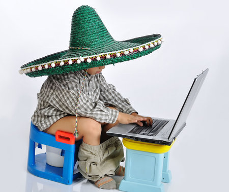 Cute kid with mexican hat on head, sitting on toilet with laptop