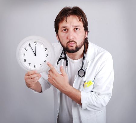  male doctor holding out an alarm clock ticking ever closer to 12 の写真素材