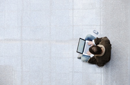 Young man sitting on the floor and  surfing on laptop with large copy-spaceの写真素材