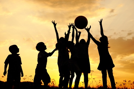 Silhouette, group of happy children playing on meadow, sunset, summertimeの写真素材