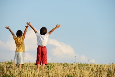 Two kids standing on meadow with arms up in airの写真素材