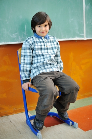 Cute little boy sitting in chair in front of blackboardの写真素材