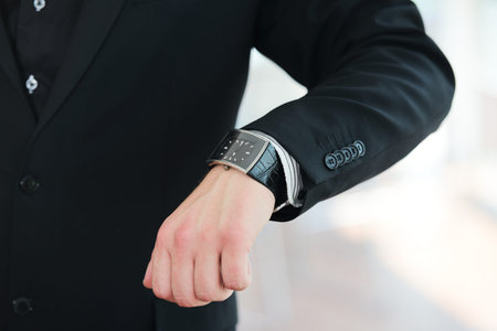 Businessman looking at clock wristwatch on hand in office