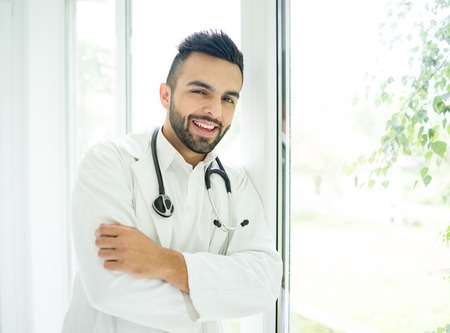 Attractive doctor with fashionable hair style standing on window and smilingの写真素材