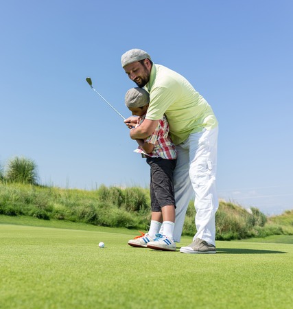Father teaching son playing golf at clubの写真素材
