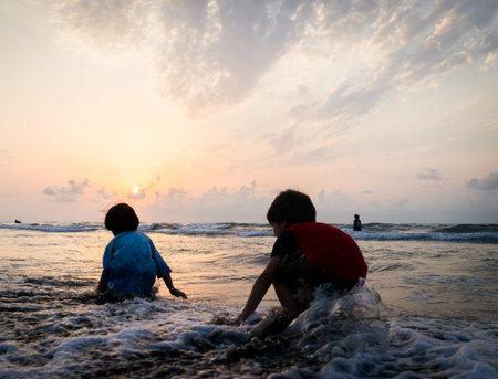 Kids silhouettes having happy time on sea beach near sunsetの写真素材