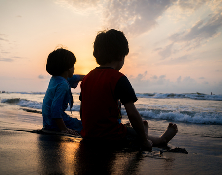 Kids silhouettes having happy time on sea beach near sunsetの写真素材