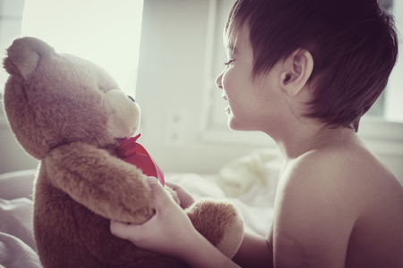 A little cute boy with Teddy bear on the bedの写真素材