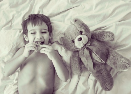 A little cute boy with Teddy bear on the bedの写真素材