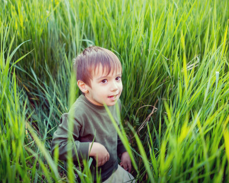 Happy kid with raised arms in green spring field against blue sky. Freedom and happiness concept