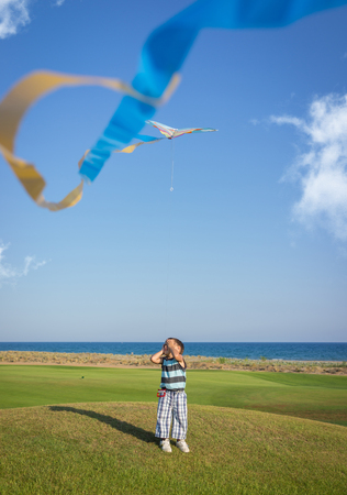Little boy on summer vacation having fun and happy time flying kite on the sea beachの写真素材