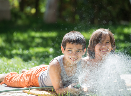 Cute little boys on summer meadow splashing water having fun and happy timeの写真素材