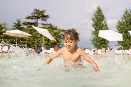 Cute little boy kid child splashing in swimming pool having fun leisure activityの写真素材