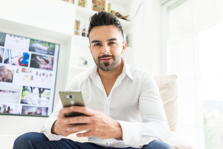 Young good looking man at home using a phoneの写真素材