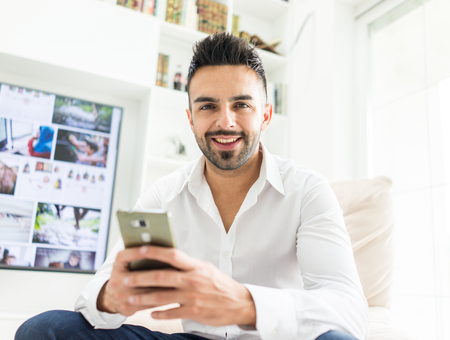 Young good looking man at home using a phoneの写真素材