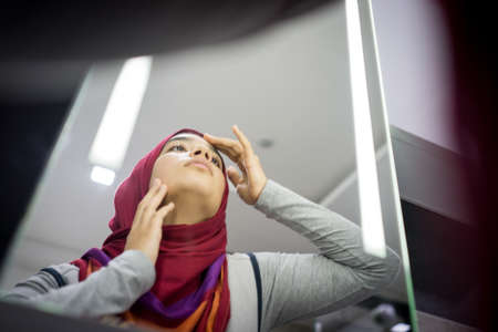 Muslim beautiful girl looking into mirror checking faceの写真素材