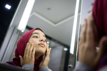Muslim beautiful girl looking into mirror checking faceの写真素材