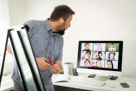 Male teacher having online conference with school children working at homeの写真素材