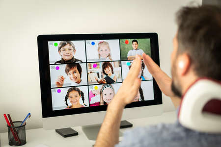Male teacher having online conference with school children working at homeの写真素材