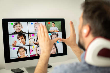 Male teacher having online conference with school children working at homeの写真素材