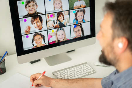 Male teacher having online conference with school children working at homeの写真素材