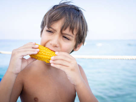Boy sitting on beach pier and eatingの写真素材