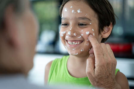 Grandmother and little boy putting cream protection on their faceの写真素材