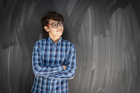Teenage boy with glasses in front of classroom chalkboardの写真素材