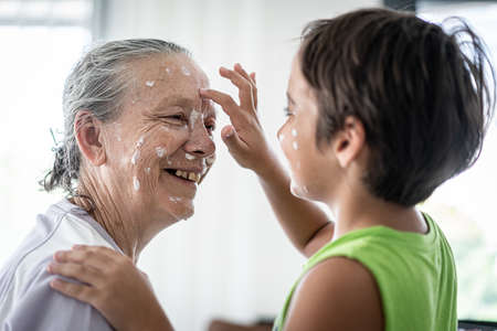 Grandmother and little boy putting cream protection on their faceの写真素材