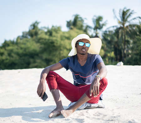 African man sitting on sandy beachの写真素材