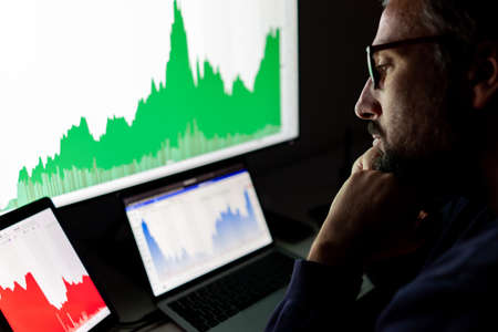 Crypto trader investor analyst looking at screen analyzing financial graph data on pc monitor, online stock exchange market ,over shoulder view.の写真素材